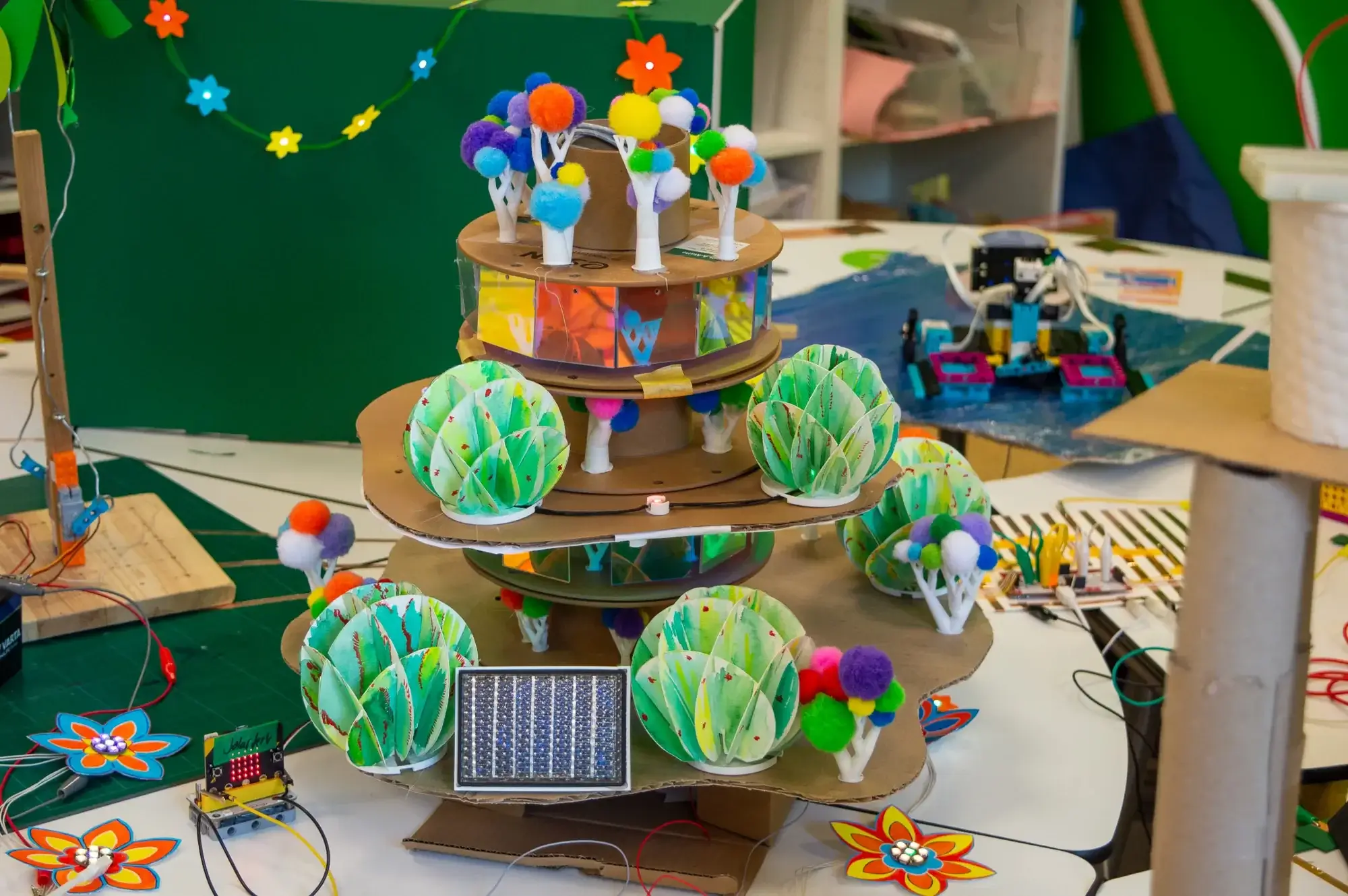 Kartonturm mit 3D-gedruckten Bäumchen, Pompons und holografischen Fenstern, am Fuß ein micro:bit